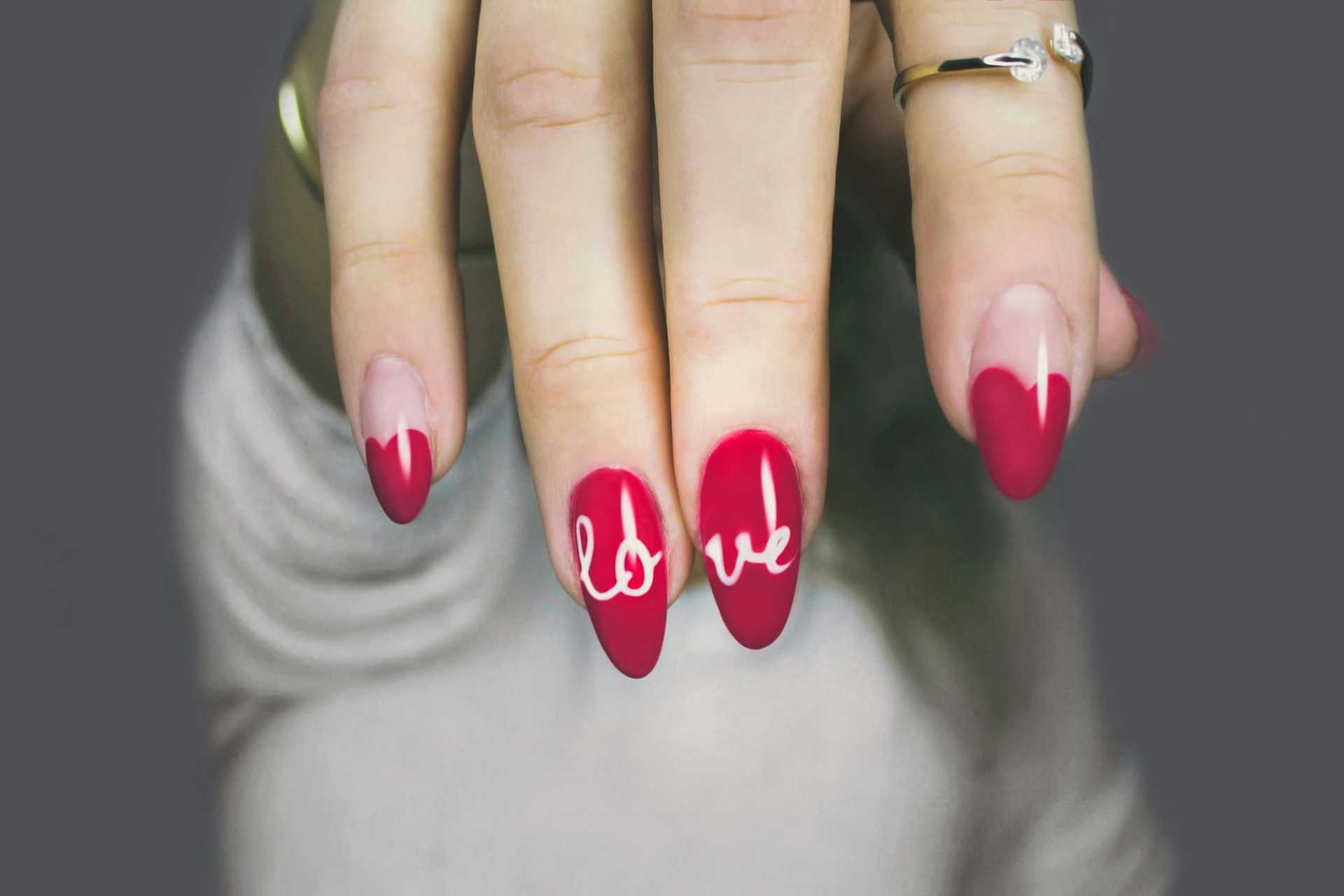 Red and pink nails spell "love" on a hand with a grey background.